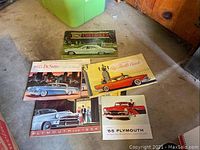 Five vintage automotive sales brochures: 1962 Chevrolet, 1955 DeSoto, Big Thrills Buick, 1954 Plymouth, '55 Plymouth laid on garage floor