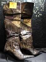 Full view of the pair of brown thigh high boots with fringe and various textures and finishes in leather and suede, showing pointed toes and spike heels.