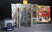 Full view of black binder with NFL trading cards in clear pages, Cowboys coffee mug, and Beckett price guide