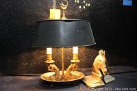 Photo showing vintage brass lamp with black shade and one brass horse head bookend on the right.