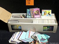 Wide angled image showing the full box of trading cards with some cards spread out and cards standing up, including card sleeves and various trading card designs visible.