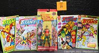 Front view of the lot including the Robin action figure in packaging centered with four colorfully illustrated New Titans comics on each side.