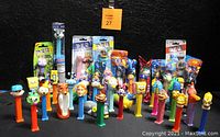 Photo showing assortment of PEZ dispensers in front of black background, some packaged with candy, various characters visible