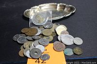 Photo showing silver-plated oval tray and assortment of diverse collectible coins and tokens spread in front and on tray against black backdrop.