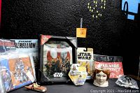 Various Star Wars collectible items displayed on black background including boxed 3D Rogue One picture, carded action figures, books, prints, and a sculpted female head bust.