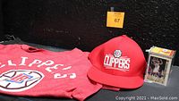 Photo showing red Clippers t-shirt, adjustable red Clippers cap, and a plastic display case containing basketball trading cards.