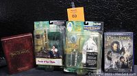Photo showing two original sealed action figures from Lord of the Rings, Gandalf the White and Frodo of the Shire, along with two Lord of the Rings DVD box sets.