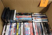Photo showing a box containing assorted DVDs stacked and arranged with visible titles such as Ocean's Eleven and Big Momma's House.