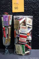 Front view of two containers filled with vintage matchbooks, showing various brand labels