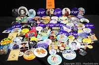 Full view of a large assortment of vintage pin-back buttons showing various celebrity, movie, and pop culture themes.