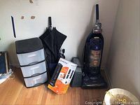 Wide view of Bissell vacuum, storage drawers, umbrellas, cardboard box, and trash can on wood floor