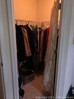 Wide view of closet with multiple vintage coats, dresses, and other clothes hung on racks