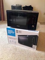 Black Samsung convection microwave oven placed on top of its original box with visible branding and features.