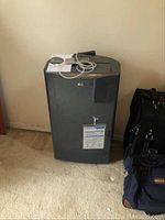 Front view of LG portable air conditioner unit placed on carpeted floor with remote and owner's manual on top.