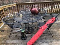 Patio table with four chairs, red umbrella in sleeve, green pedestal stand, red watering can on deck