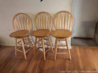 Front view of three wooden bar stools with rounded backs, positioned side by side on hardwood floor.