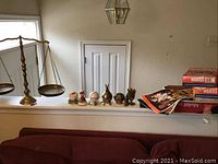 Full view of the brass balance scales, signed baseballs, Charlie Brown music player, brass bowls, Orioles pennants, and Wheaties boxes laid out on a ledge.