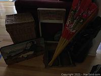 Photo shows wicker hamper, vintage washboard frame, large red folding fan, coat rack, spoon rack, and can crusher bin arranged near couch.