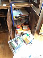 Photo of wooden cabinet filled with various paper notepads, stacks of books, and boxes containing paper goods and CDs.