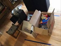 Overview of lot showing footstool, small cabinet, cardboard boxes with various supplies including candle molds and paper products.