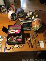 Overall view of lot on wooden table showing eggs, tray, pens, watches, jewelry box and assortment