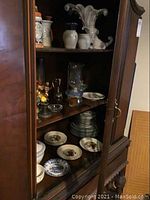 Wooden cabinet with assorted plates and decorative items, shows arrangement and condition of lot pieces.