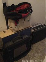 Overview of lot showing multiple luggage pieces including blue and beige hard sided luggage, black briefcase, black soft case and red/black The North Face backpack stacked