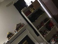Photo showing white shelving unit with multiple Christmas decor items including a skull decoration, nativity figurines on mantel, boxes, and various holiday decorations stored on shelves.