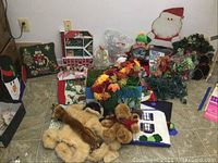 Wide view of Christmas decor items on floor showing pillows, wooden characters, flowers, stuffed animals and linens