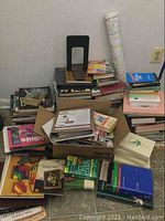 Wide view of assorted books piled on the floor with various subjects visible including cookbooks, crafts, and collector guides.