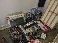 Overview of shelf with assorted VHS tapes, Video CopyMaster duplicator, jigsaw puzzle, trivia book, and body shaper products.