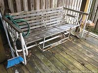 Full view of the patio glider showing white metal frame and wooden slats, with garden hose draped over it on wooden deck