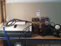 Photo showing Canon i860 printer on shelf with some cables, Panasonic electric pencil sharpener, clip light, and USB cables in packaging beside printer.