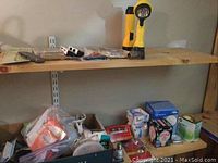 Shelf with a variety of items including two yellow flashlights, assorted hardware, plastic bucket, paint can, and scattered smaller tools and parts.