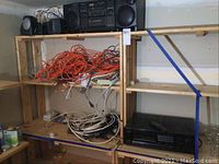 Shelf with Sony portable stereo CFD510 on top with black speakers, orange and white cables and cords on middle shelf, and more black electronic device on bottom shelf.