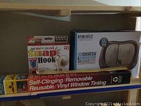 Photo of the Homedics 3D Shiatsu massager in its retail box, Snap Hook package, vinyl window tinting roll, and wooden back scratcher. The massager box is beige and brown with product details.