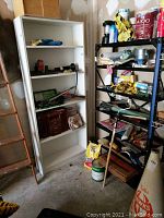 View of white wooden shelving unit with assorted tools, gloves, hand tools, and a tool belt box on top, seen near metal shelving with painting items