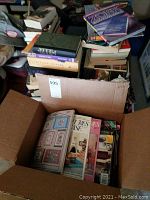 Cardboard box filled with assorted magazines and books, including visible sewing and dollhouse magazines.