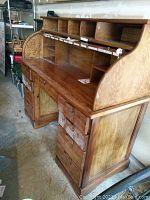 Side angle showing multiple drawers and roll top cover on the right side, with keyhole and wood grain.