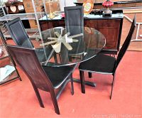 Photo showing set of four black Italian dinette chairs around round glass table with decorative cast metal base, minor scratches visible, stored indoors.
