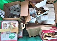 Box lot showing key blanks in white boxes labeled H SEC, door lock assemblies in packaging, and miscellaneous hardware parts tightly packed in a tote.
