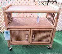 Front view showing the rattan frame, woven rattan shelves, and double-door cabinet beneath, all on caster wheels.