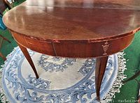 Close-up of antique wood table surface showing the rounded end, scratches, aging, and inlay decoration on apron.