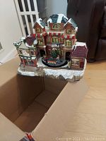 Photo of Lemax Jewelers Village Christmas house on snowy base with detailed decorations and miniature figures, showing the front facade and attached train gondola on rail track.