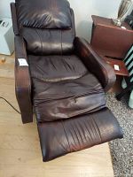 Full view of the dark brown leather electric recliner chair with extended footrest, showing some wear on the seat and armrests.