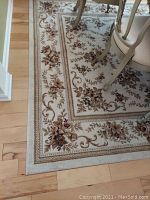 Close up corner view showing floral border and tan base color of the rug.