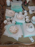 Overview photo displaying multiple stacks of plates, cups, saucers, and bowls arranged on a table with protective napkins in between pieces.