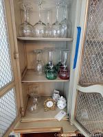 Cabinet shelf with 17 assorted glass goblets of various sizes and colors, Villeroy and Boch cream and sugar set, small wind-up globe clock on lower shelf
