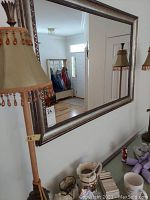 Photo showing the mirror hung on a wall with its wide decorative metallic frame and reflection of hallway