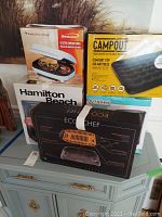 Brentwood grill, Hamilton Beach coffee maker, Kitchen Electives coffee machine, EcoChef indoor grill, Camp Out air mattress all boxed and stacked